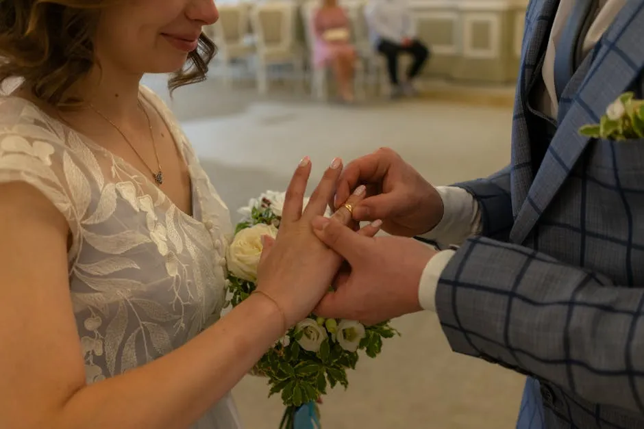 From above of crop unrecognizable man in stylish suit putting golden ring on hand of smiling bride during wedding ceremony