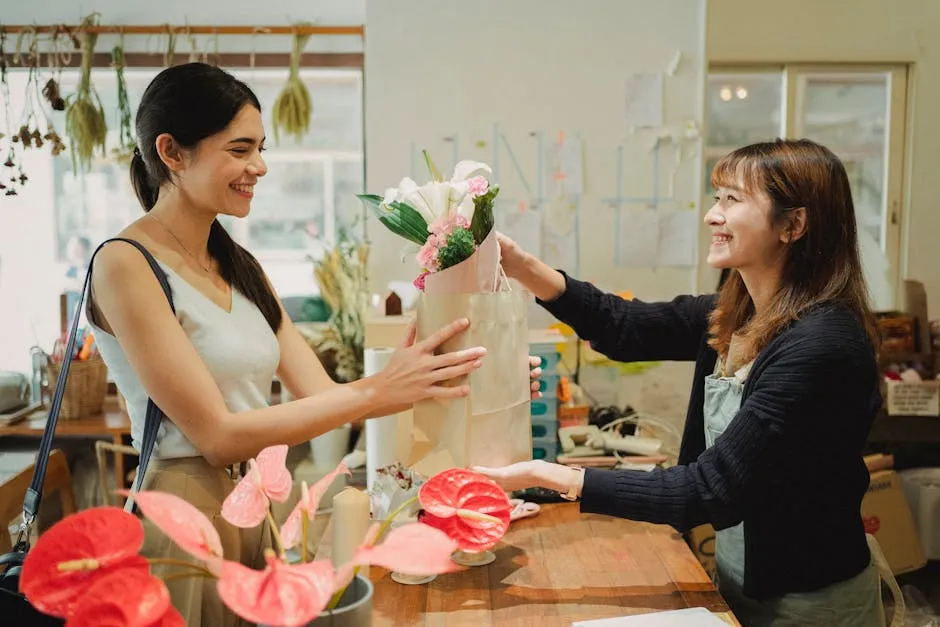 Side view of cheerful florist in apron giving paper bag with bouquets of flowers to smiling customer in floral shop in daytime