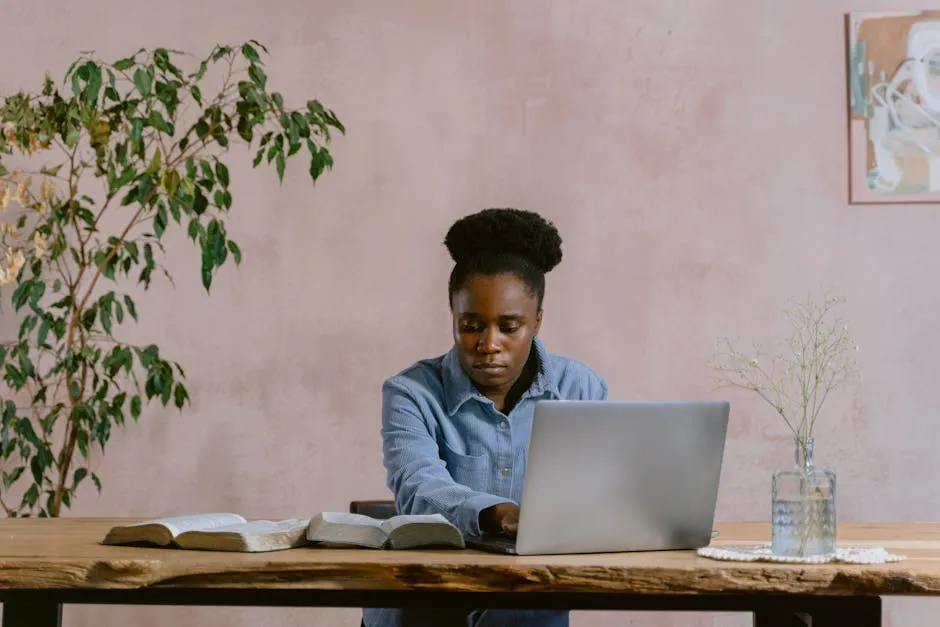 Woman in Blue Dress Shirt Reading a Bible While Typing