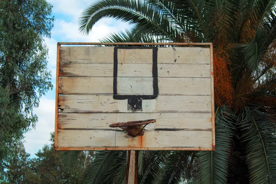 A vintage basketball hoop sits outdoors surrounded by palm trees, exuding a tropical vibe.