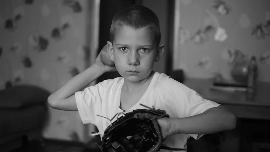 A focused young boy practicing baseball indoors in a monochrome setting.