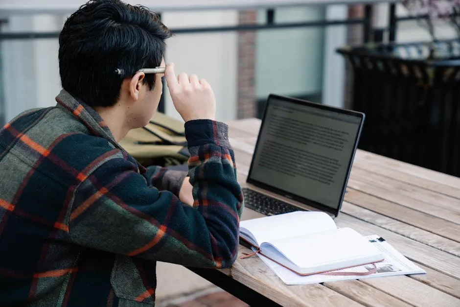 A student studies with a laptop and notebook outdoors, reflecting modern learning.