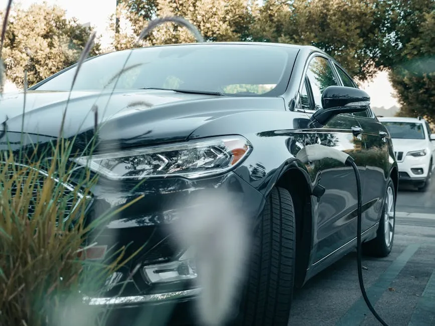 A black hybrid car charging at an outdoor station surrounded by greenery.