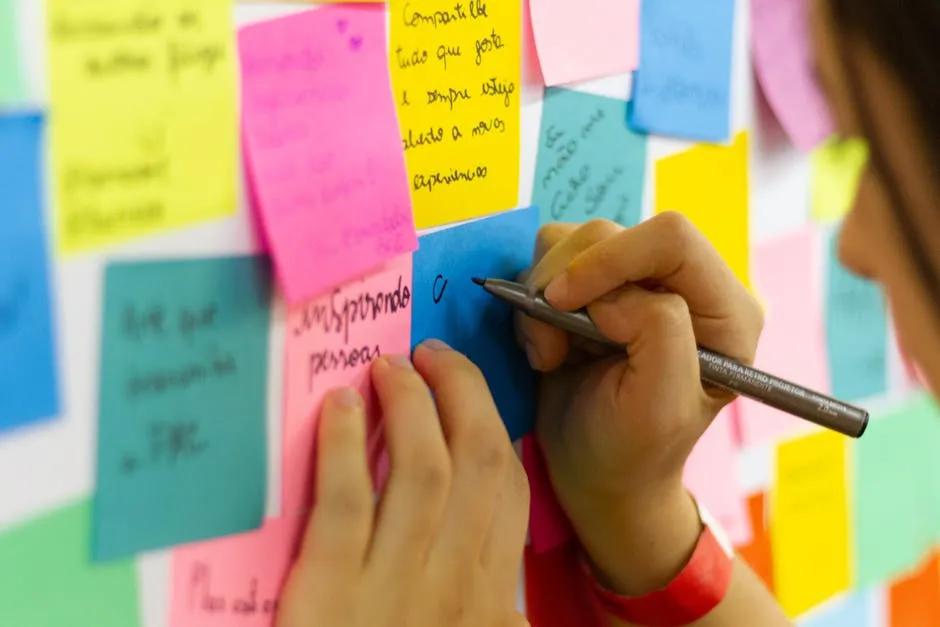 Hands writing on colorful sticky notes during a brainstorming session indoors.