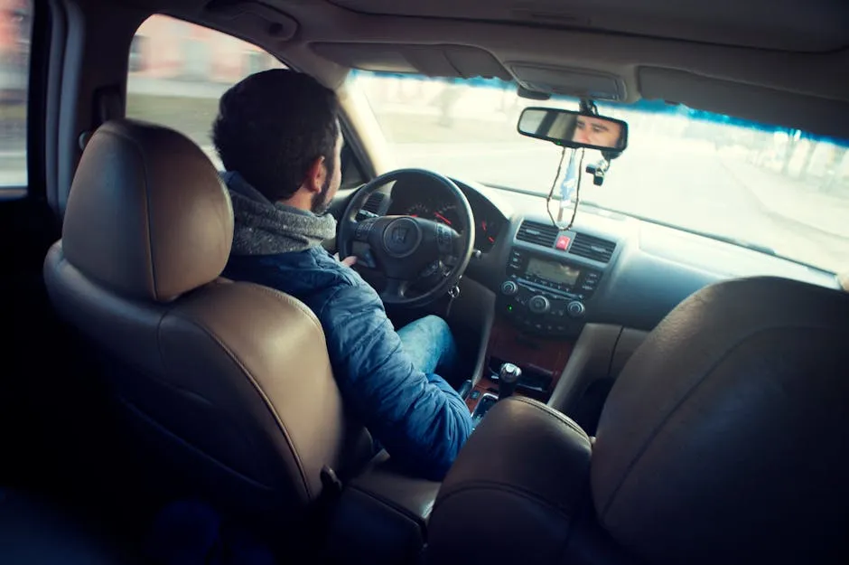 A man driving a car with focus on interior, dashboard, and steering wheel, captured from the backseat.